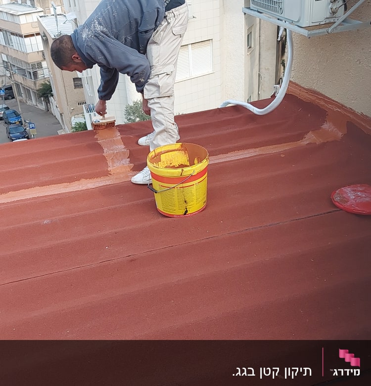 אדם מורח חומר איטום על גג בעזרת מברשת